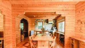A wooden cabin interior with a central dining table, kitchen area, and large windows. - Lodge Kent (Hokuto)
