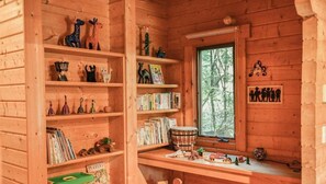 A cozy cabin interior with wooden shelves filled with books, puzzles, and toys. A window with a view of trees is visible. - Lodge Kent (Hokuto)