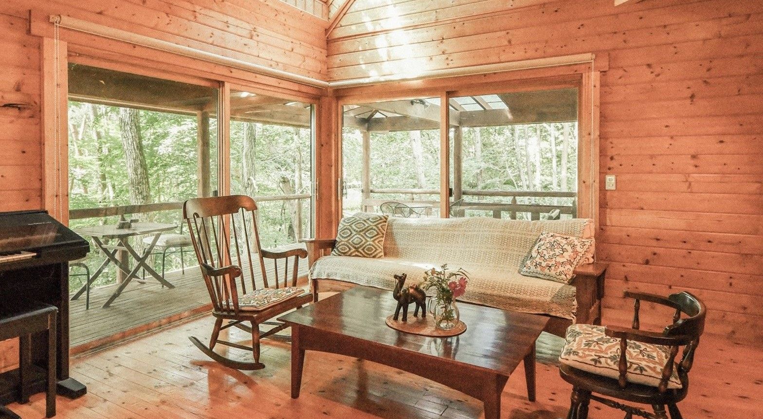 A cozy cabin interior with a wooden floor, a sofa, rocking chairs, and a table with a decorative item.