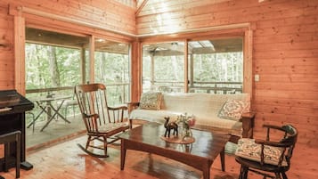 A cozy cabin interior with a wooden floor, a sofa, rocking chairs, and a table with a decorative item.