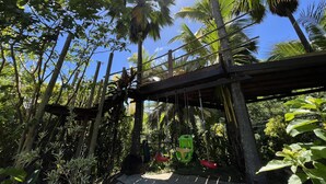 Una terraza de madera con un columpio, rodeada de exuberante vegetación tropical y palmeras.
