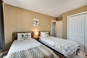 Een slaapkamer met twee eenpersoonsbedden, een nachtkastje met een lamp, een schilderij aan de muur en een deur aan de rechterkant.
