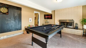 Een biljart in een ruimte met een dartbord, een open haard en een televisie waarop 'NETFLIX' staat.