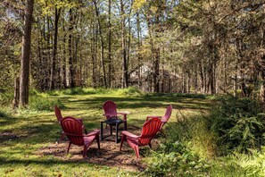 Een bebost gebied met een kleine tafel en twee Adirondack-stoelen.