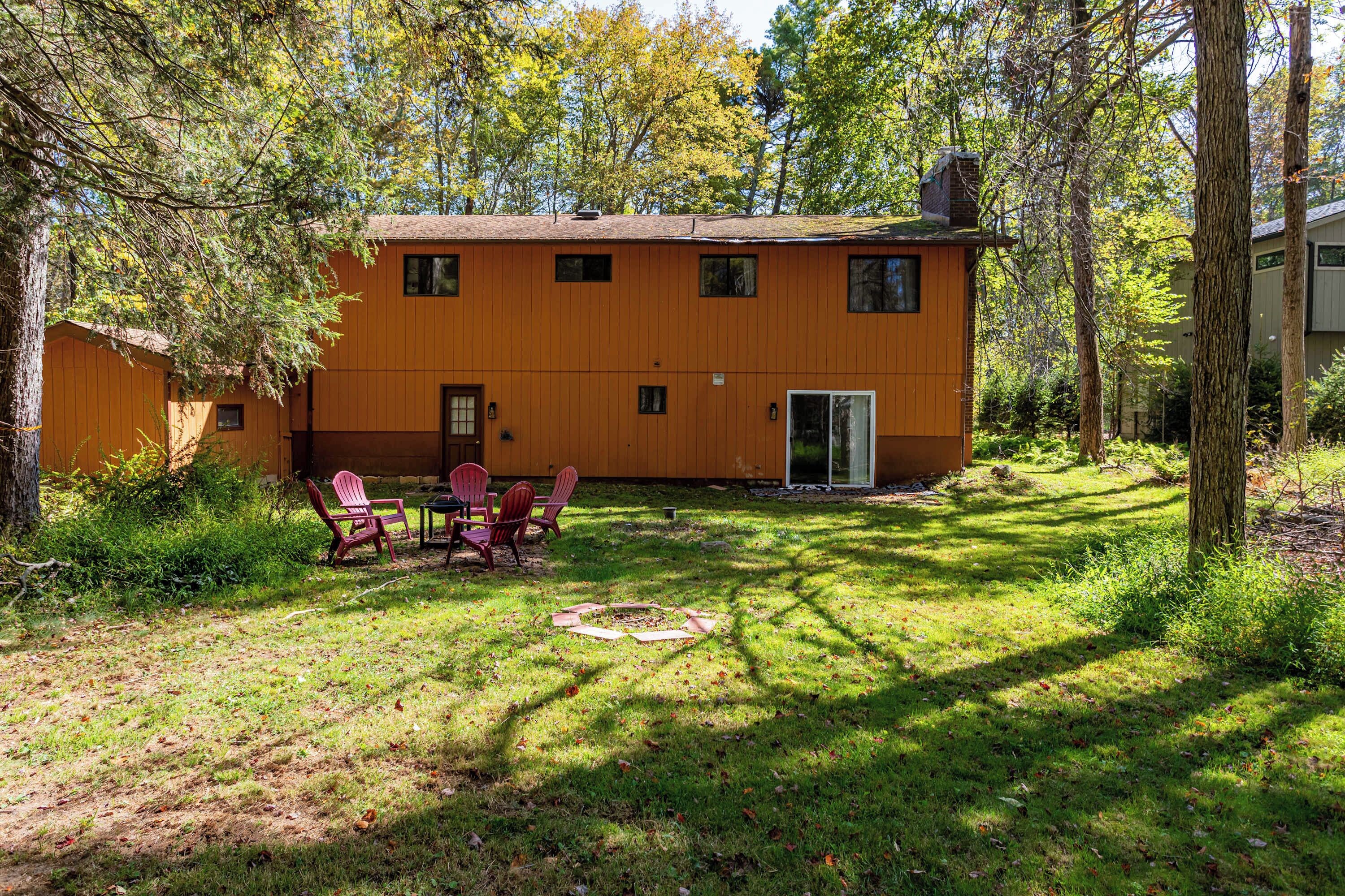 A two-story building with a wooden exterior, a front door, and a small porch with red chairs.
