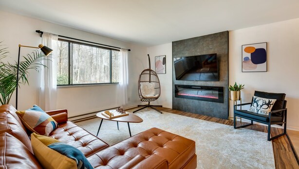 Een moderne woonkamer met een leren bank, een hangstoel, een open haard en een grote televisie.