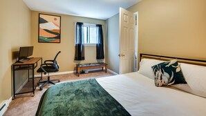 Hotelkamer met een bed, bureau met computer, stoel, raam met gordijnen en een deur.