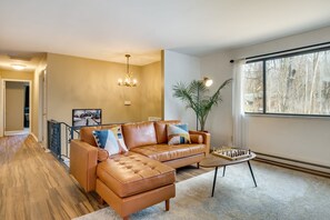 A living room with a brown leather sofa, a coffee table, and a large window with a view of trees. - Lake Naomi Home w/ Game Rm, Fire Pit, Dogs (Pocono Pines)