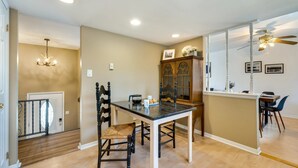 A dining area with a black table, four chairs, a chandelier, a wooden cabinet, and a ceiling fan.