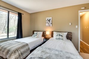 A room with two beds, a window with curtains, a wall-mounted lamp, and a painting. - Lake Naomi Home w/ Game Rm, Fire Pit, Dogs (Pocono Pines)