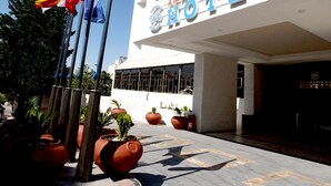 Das Aman Paradise Hotel mit moderner Fassade, mehreren Flaggen und Topfpflanzen.