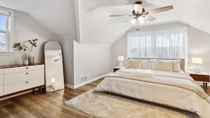 A bedroom with a bed, nightstands, a ceiling fan, a large mirror, and a window with curtains.