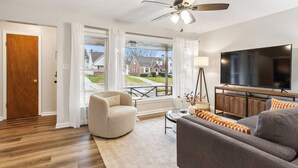 A living room with a ceiling fan, a large TV, a sofa, and a chair.