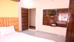 A hotel room with a bed, a television mounted on the wall, a wooden door, and a light-colored floor. - Smilestay Karanji Paradise (Bengaluru)