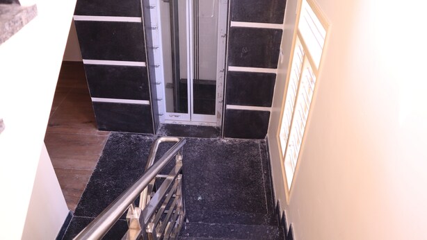 A staircase with black marble steps and a metal handrail, leading to a door with a glass panel. - Smilestay Karanji Paradise (Bengaluru)