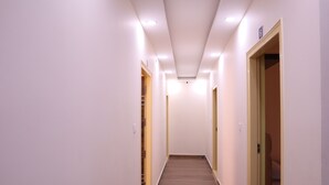 A narrow, well-lit hallway with wooden flooring and white walls. - Smilestay Karanji Paradise (Bengaluru)