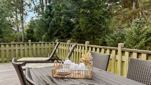 A wooden deck with wicker furniture and a table set with plates, cups, and a vase. - 3 bedroom nice home in Nexø (Nexø)