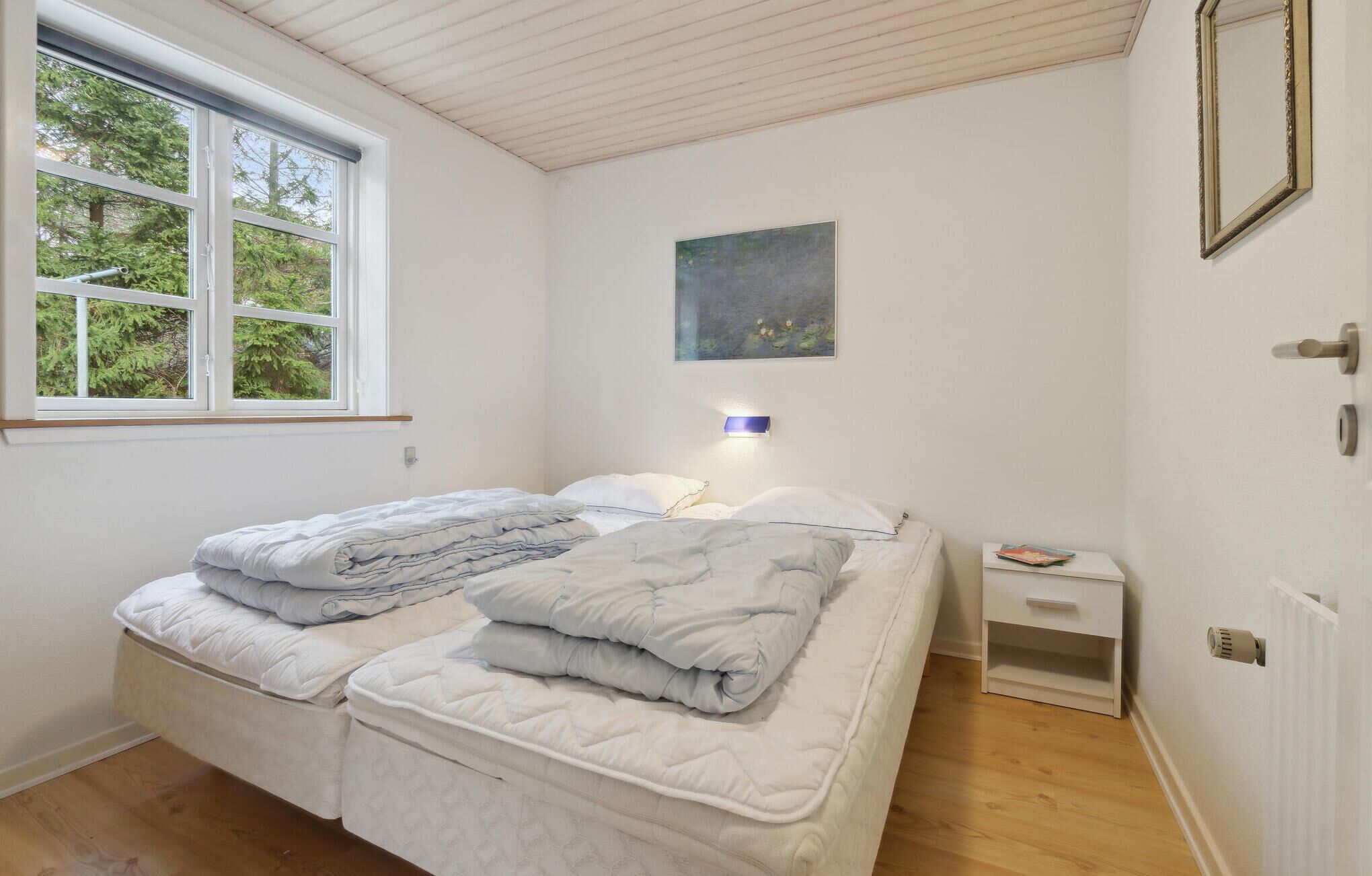A bedroom with two beds, a window, a painting, a bedside table, and a nightstand.