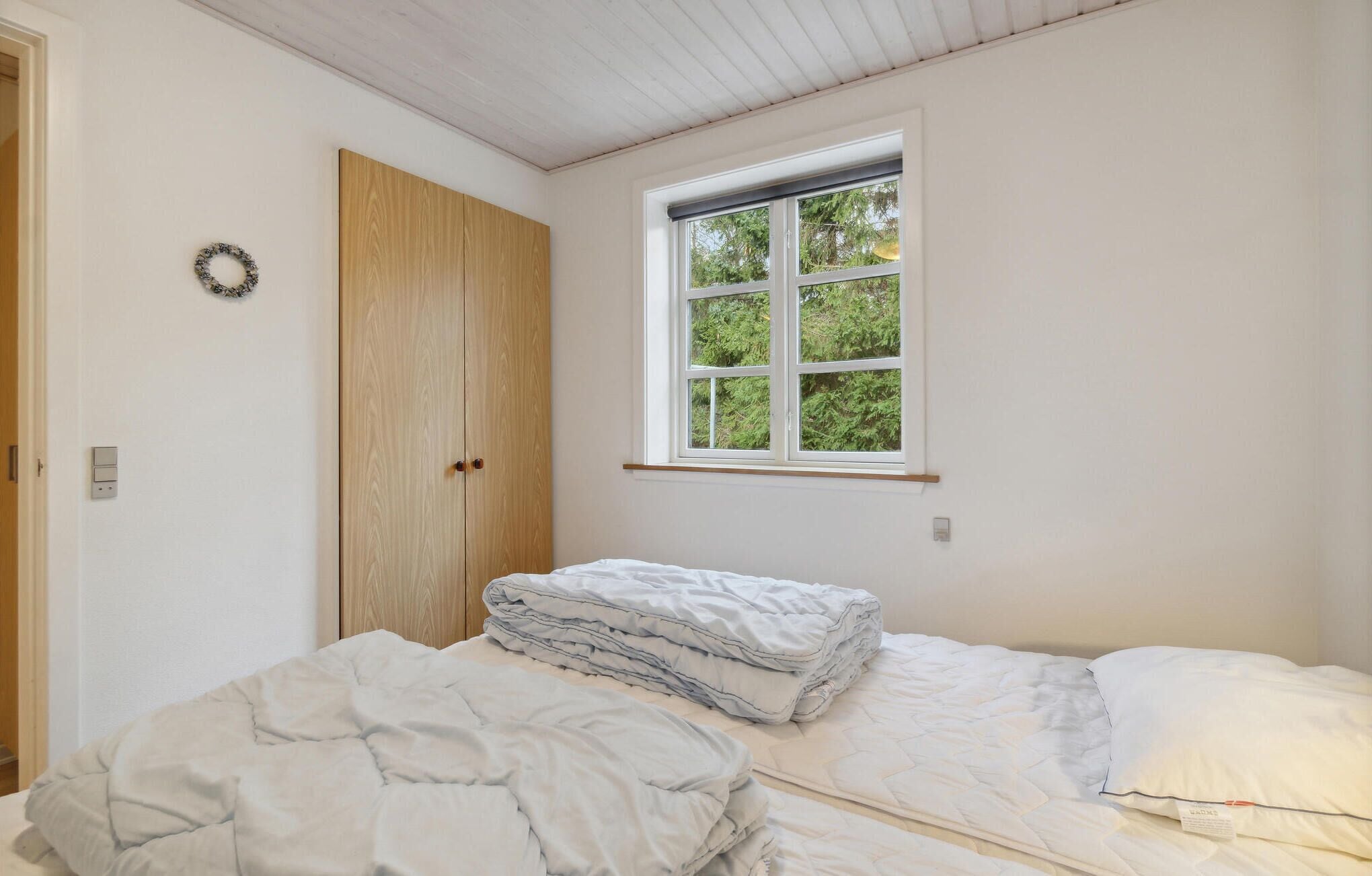 A bedroom with a wooden wardrobe, a window with a view of trees, and a bed with a folded blanket.