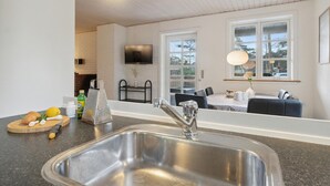 A modern kitchen with a stainless steel sink, a dining area with a table and chairs, and a TV mounted on the wall. - 3 bedroom nice home in Nexø (Nexø)