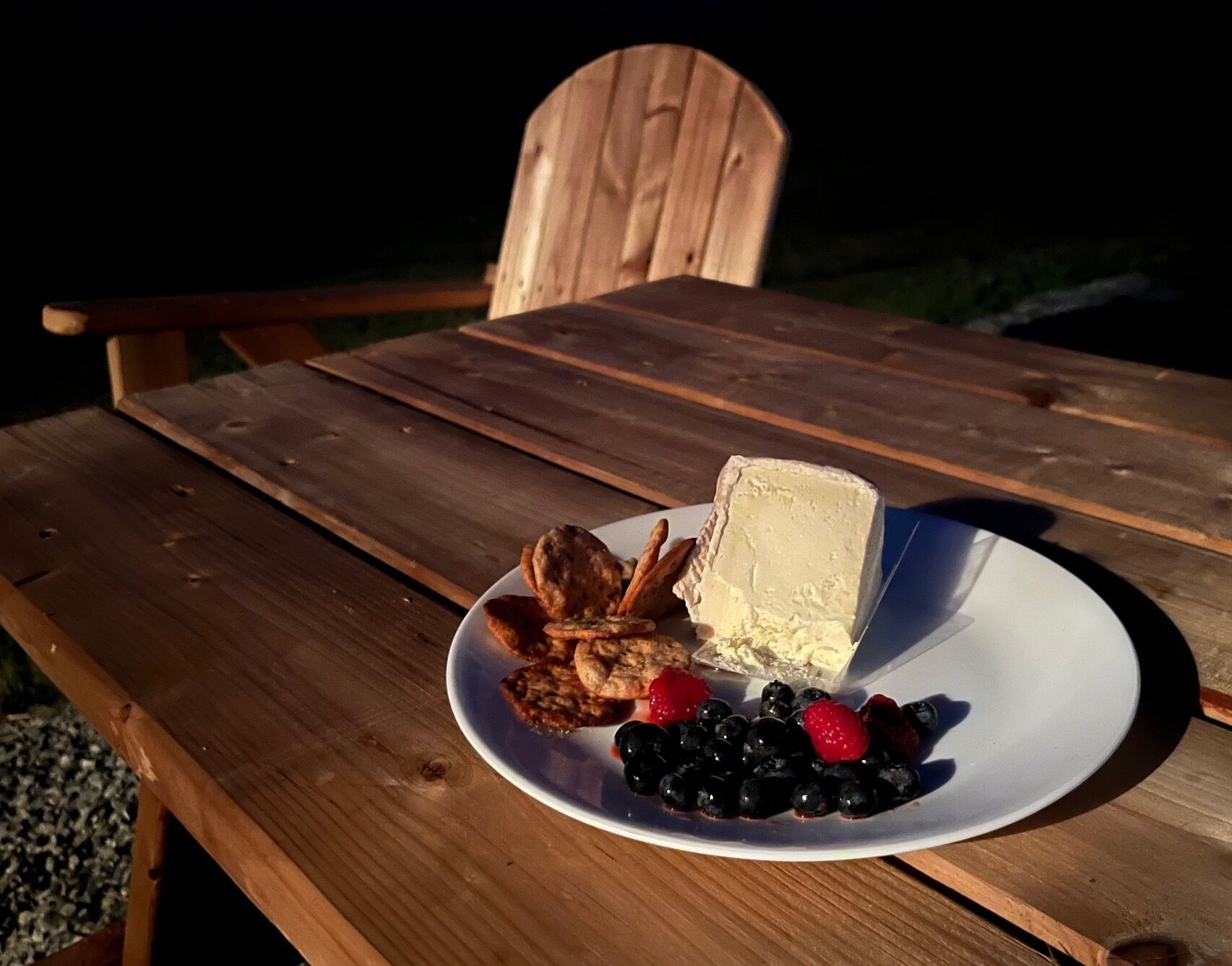 Una mesa de madera con un plato de comida que incluye queso, galletas y bayas.