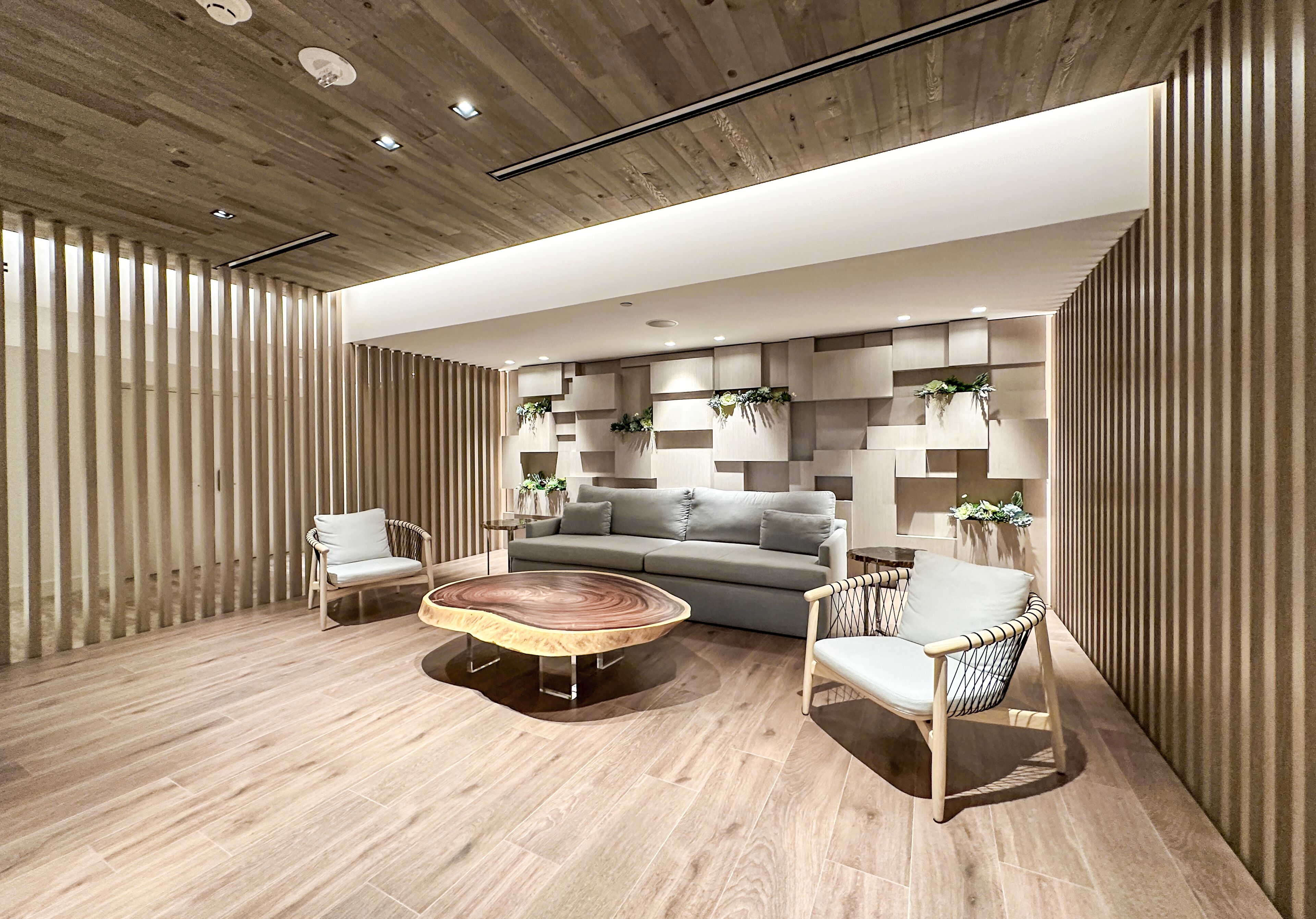 Una sala de estar moderna con un sofá gris, dos sillones, una mesita de centro y piso de madera.