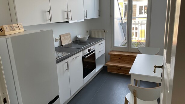 A compact kitchen with white cabinets, a built-in oven, a stovetop, and a window overlooking the street. - Gemütliche Wohnung in Berlin Mitte (Berlin)