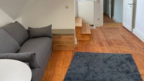 A modern loft apartment with a sloped ceiling, a grey sofa, a round white table, and a dark blue rug. - Gemütliche Wohnung in Berlin Mitte (Berlin)