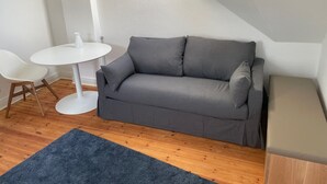 A small, modern room with a grey sofa, a white round table, and a blue rug. - Gemütliche Wohnung in Berlin Mitte (Berlin)