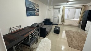 A modern living room with a dining area, a sofa, a coffee table, and a painting on the wall. - Charming 1-bed Apartment in Chigwell (Chigwell)