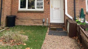 A two-story brick house with a white front door, windows, and a small porch area. - Charming 1-bed Apartment in Chigwell (Chigwell)