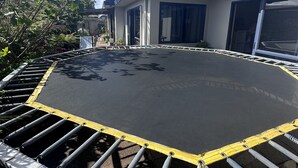 A trampoline with safety railings, surrounded by greenery and a building with large windows. - Comfortable family home, Privacy & convenience, pets welcome! (Papamoa)