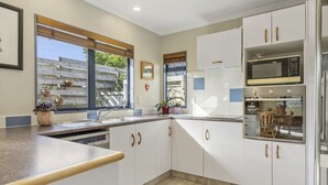 A modern kitchen with white cabinets, a built-in oven, and a large window providing natural light. - Comfortable family home, Privacy & convenience, pets welcome! (Papamoa)