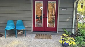A house with a red door, two blue chairs outside, and a small garden with yellow flowers.