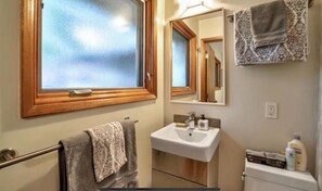 Un baño con ventana, lavabo, espejo y toallero.
