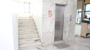 A staircase leading to an elevator in a building with marble walls and a "No Drugs" sign. - Smile stay Karanji Comforts (Bengaluru)