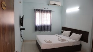 A hotel room with a bed, a TV mounted on the wall, an air conditioner, and a window with curtains. - Smile stay Karanji Comforts (Bengaluru)