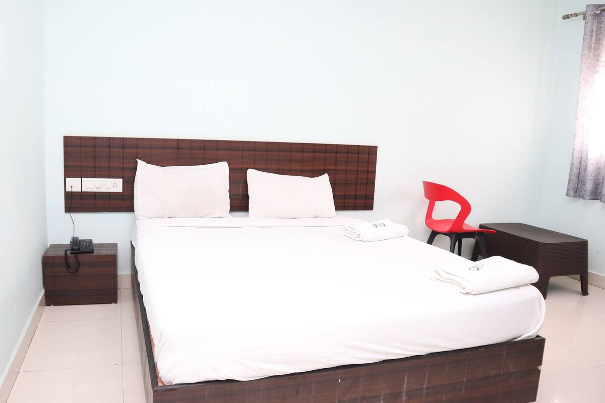 A neatly made bed with white linens, a wooden headboard, a bedside table with a phone, and a red chair.