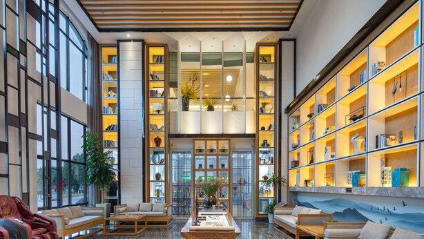 Un hall d’entrée spacieux avec un plafond haut, un espace salon central et une grande bibliothèque remplie de livres et d’objets décoratifs.