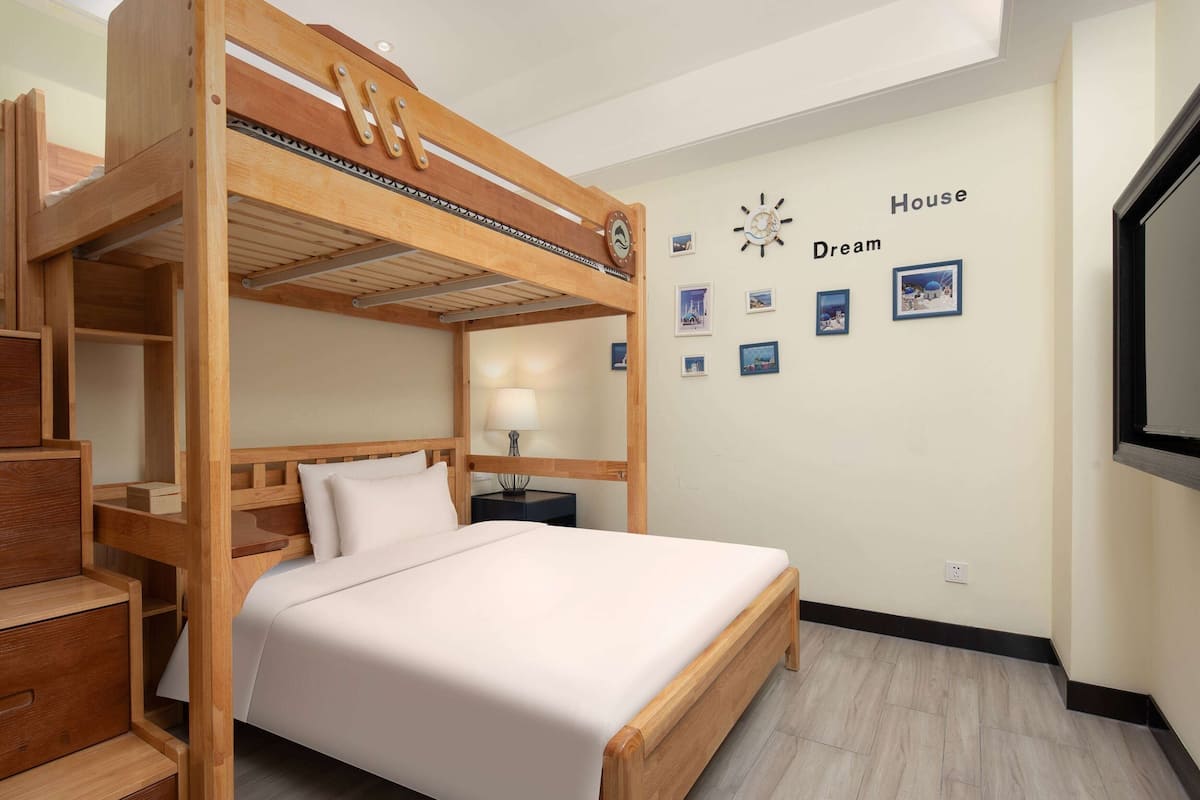 A bunk bed room with a wooden headboard, a bedside table with a lamp, and a wall with framed pictures and the words "House Dream".