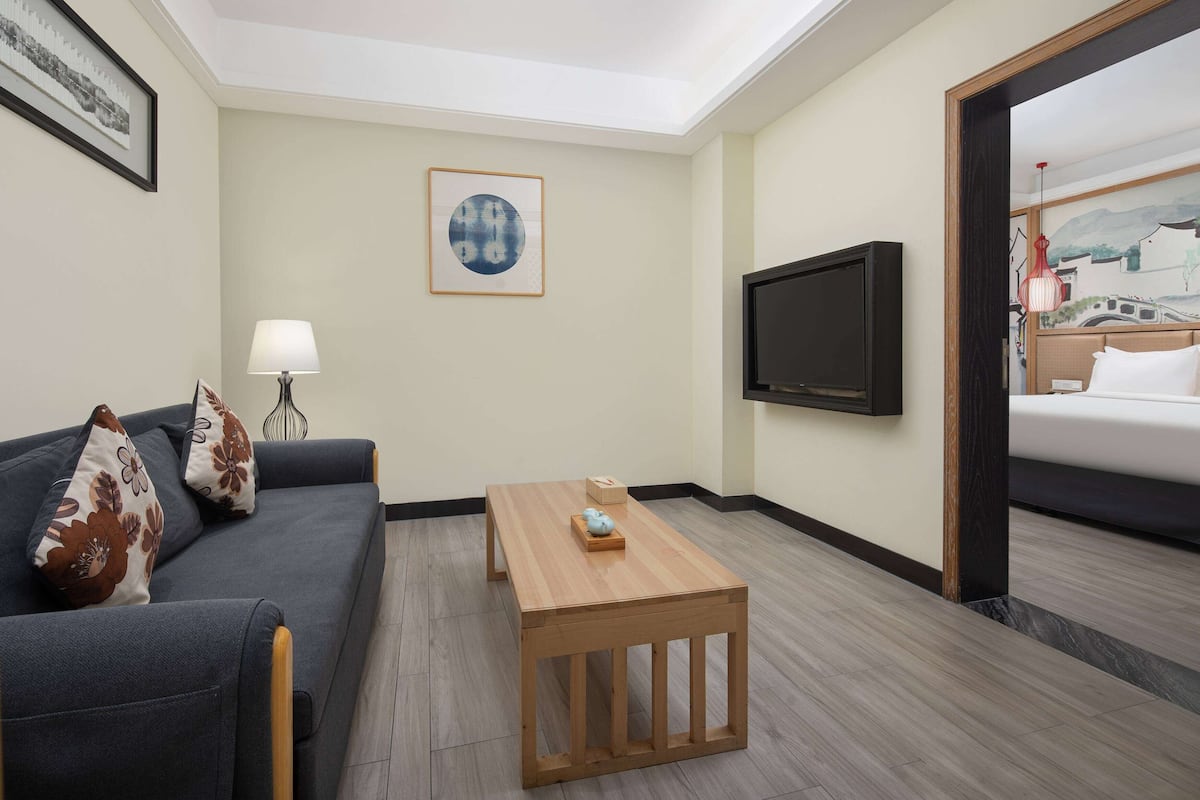A hotel room with a sofa, a wooden coffee table, a TV, and a bed.