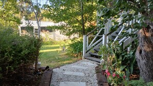Un sendero que lleva a una escalera de madera rodeada de follaje y un edificio al fondo.