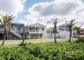 Un edificio moderno de dos pisos con un balcón, rodeado de exuberante vegetación y palmeras.