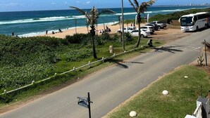 A coastal road with a beach, palm trees, and a bus. - On The Beach (Durban North)