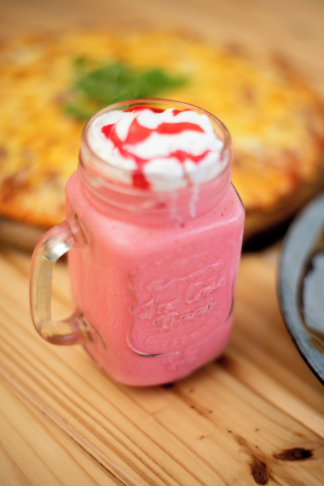 A pink smoothie in a glass mug with a handle, placed on a wooden surface.