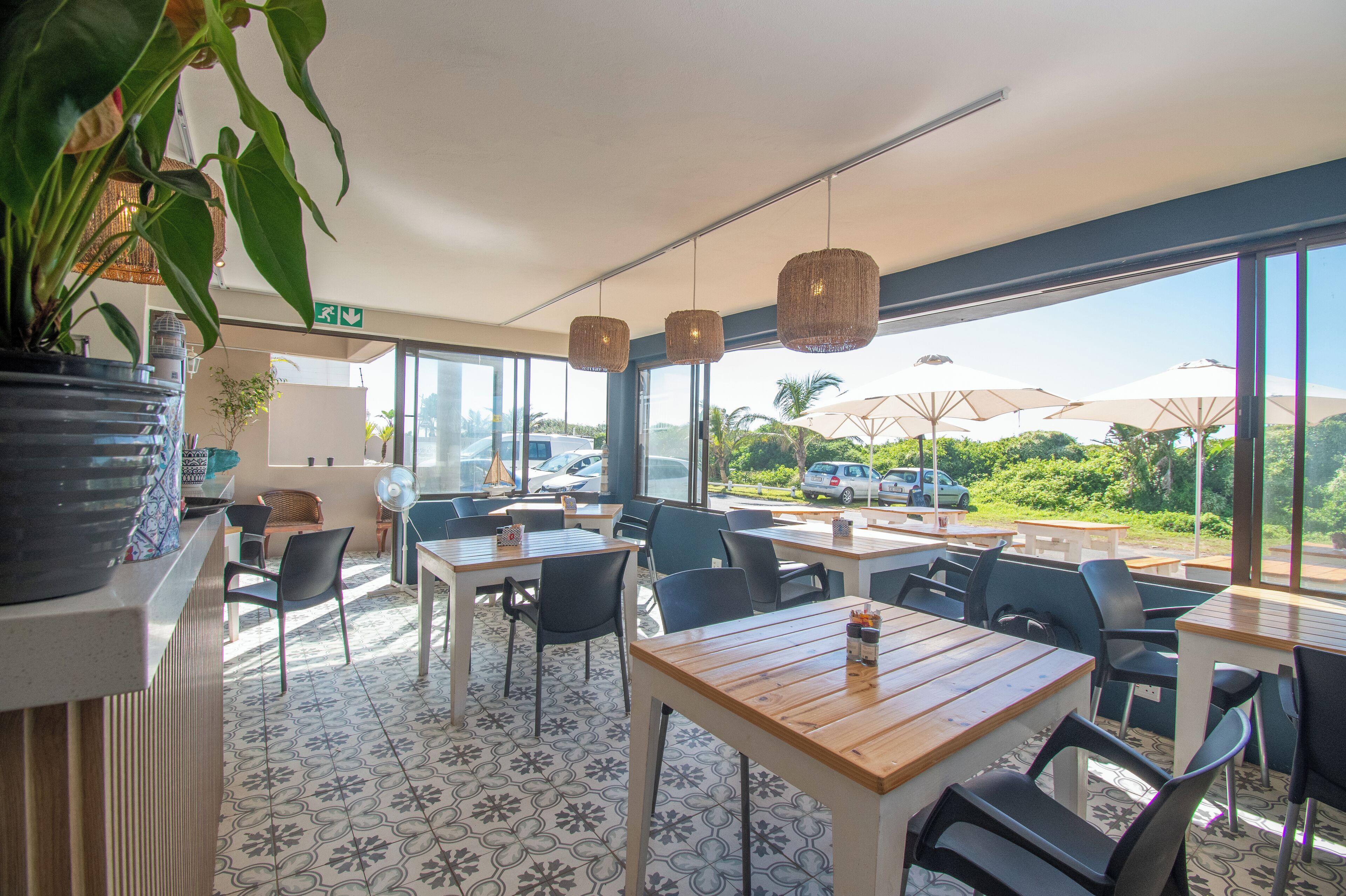 A restaurant with outdoor seating, large windows, and a view of the parking area.