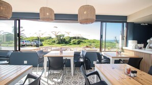 A restaurant with outdoor seating, large windows, and a view of the ocean. - On The Beach (Durban North)
