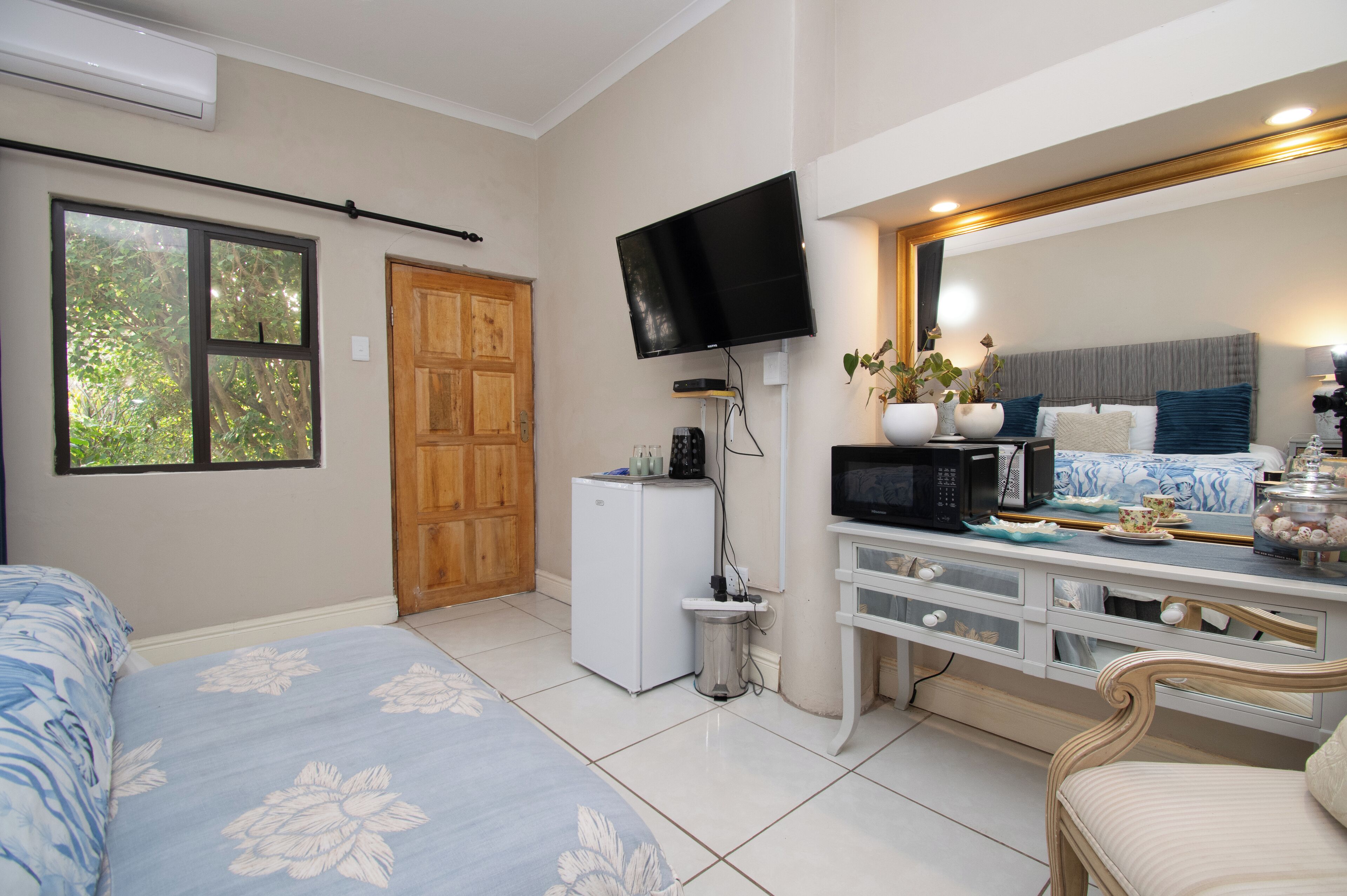 A bedroom with a bed, a desk with a TV, a microwave, and a small fridge.