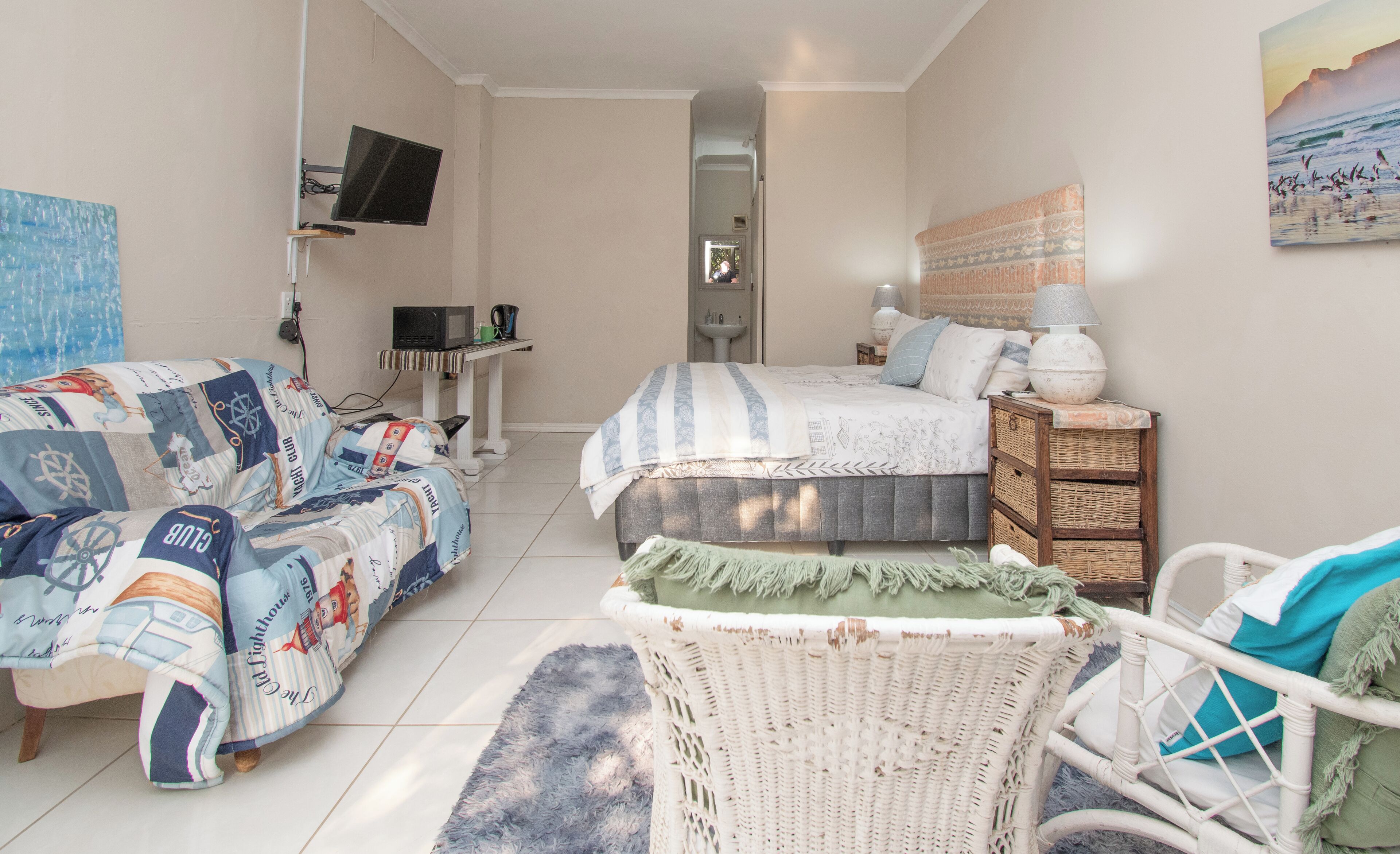 A bedroom with a bed, a sofa, a chair, a television, and a painting on the wall.