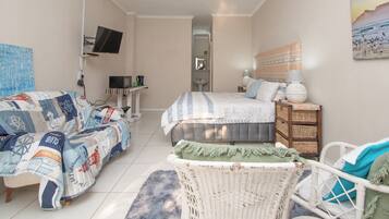 A bedroom with a bed, a sofa, a chair, a television, and a painting on the wall.